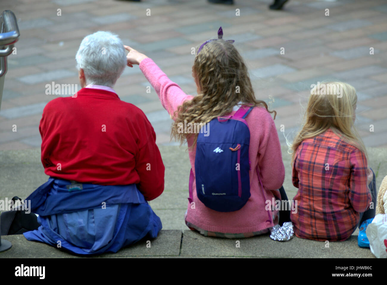 white granny and grandchildren sitting on the steps having lunch at the royal concert hall Glasgow pointing left Stock Photo