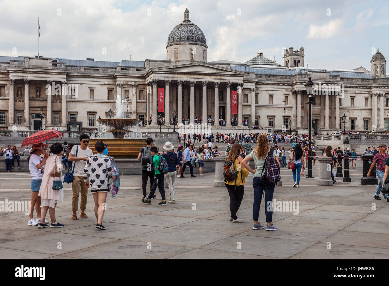 Tourists and locals standing and sitting outside the National Gallery on Trafalgar Square, London,  Relaxing, chatting, checking phones, taking photog Stock Photo