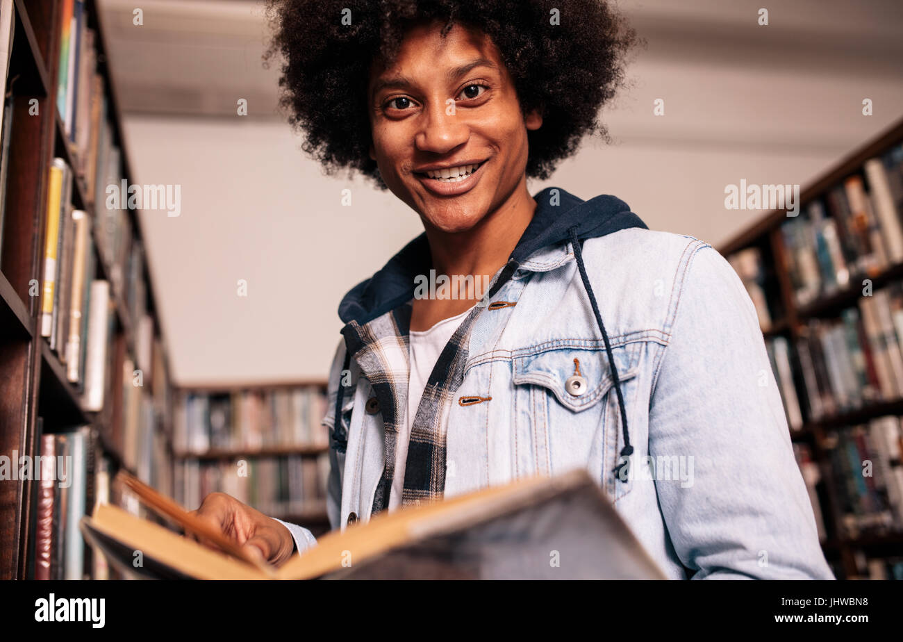 Young black man holding a book and looking at camera. University student reading book in library. Stock Photo