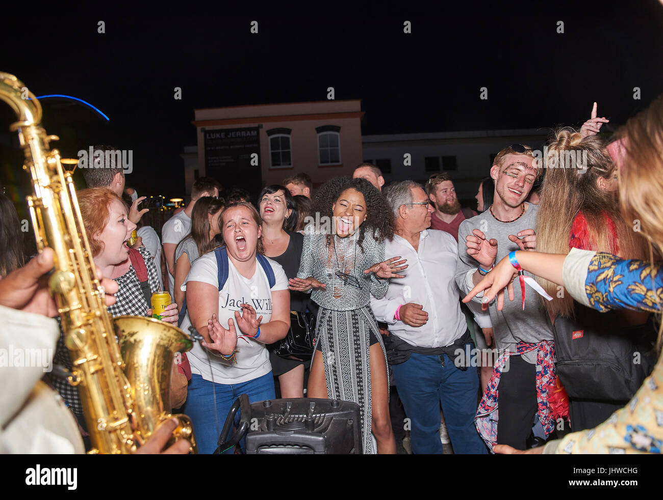 BRISTOL, ENGLAND - JULY 8: Men and women dance and sing as a Saxophonist busks at night at Bristol Waterfront on July 8, 2017 Stock Photo