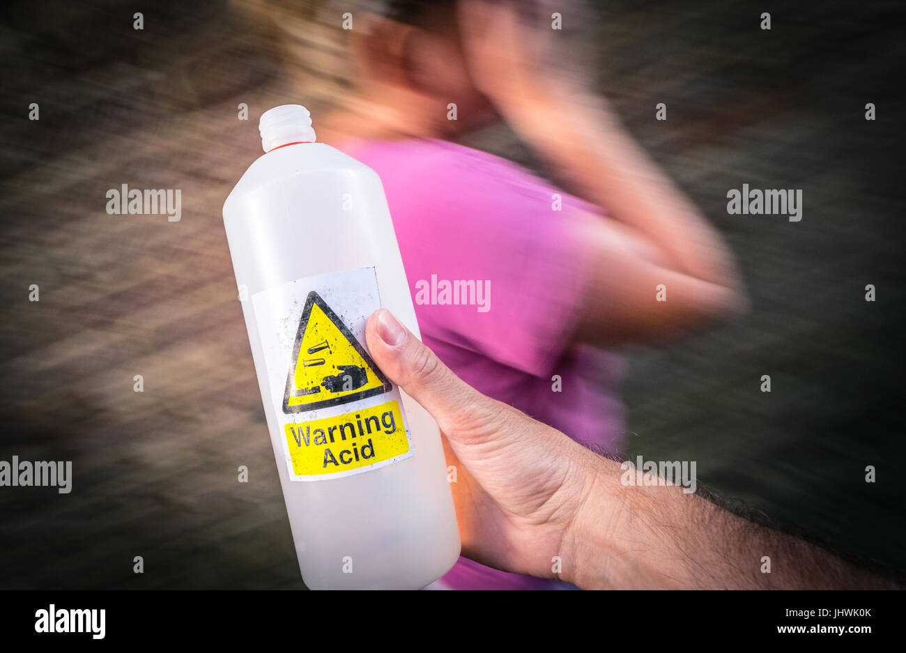Acid Attack, A man holding an acid bottle in the street near a passing woman Stock Photo