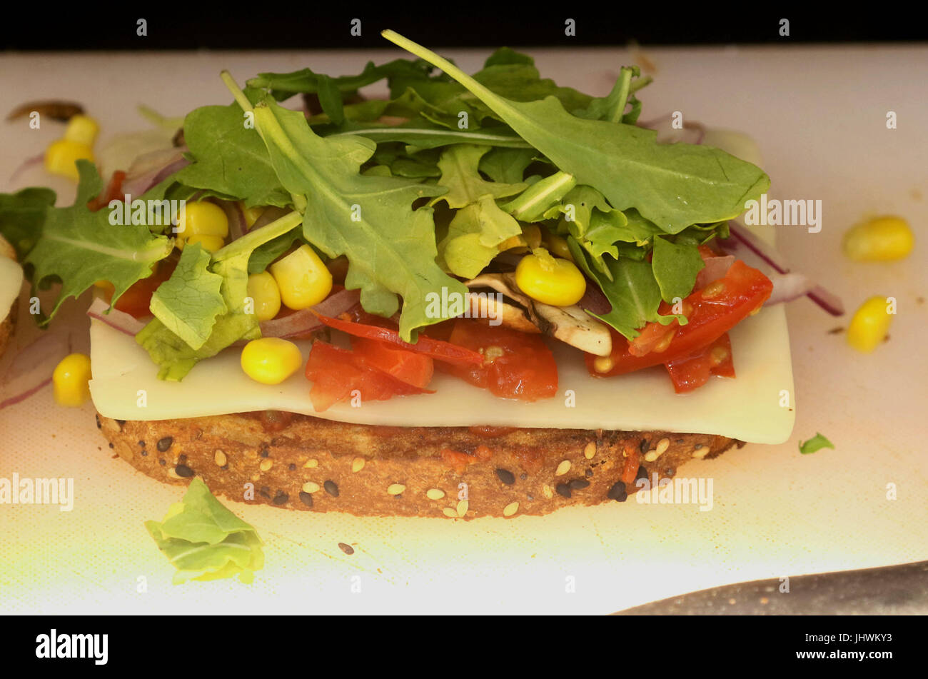 Food preparation with a piece of multigrain bread, slice of mozzarella, lettuce, tomato and corn Stock Photo