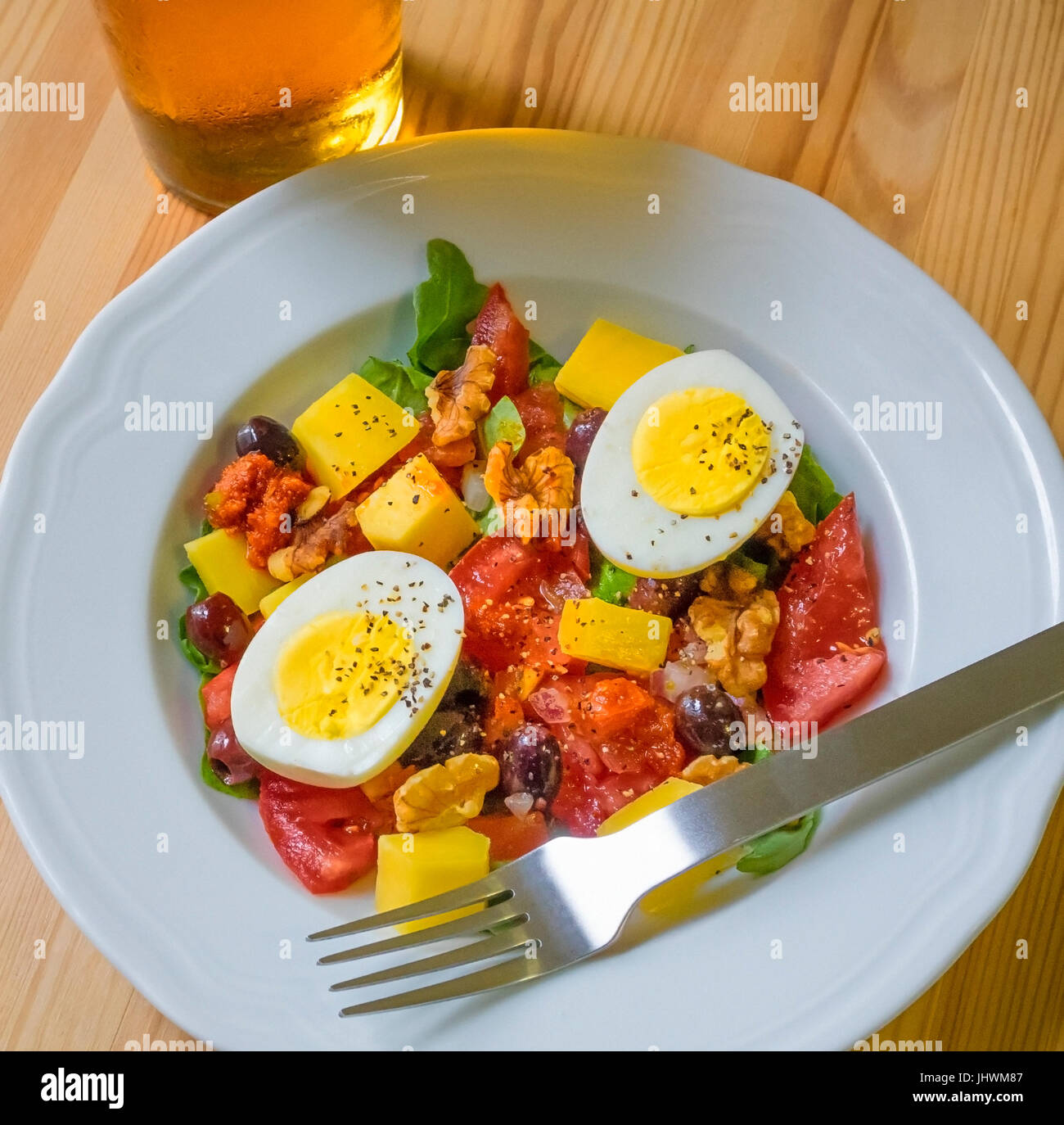 Dinner salad, with hard-boiled egg, tomatoes, cheddar chess, olives, walnuts, salsa fresca, baby arugula, and a cool pint of larger beer Stock Photo
