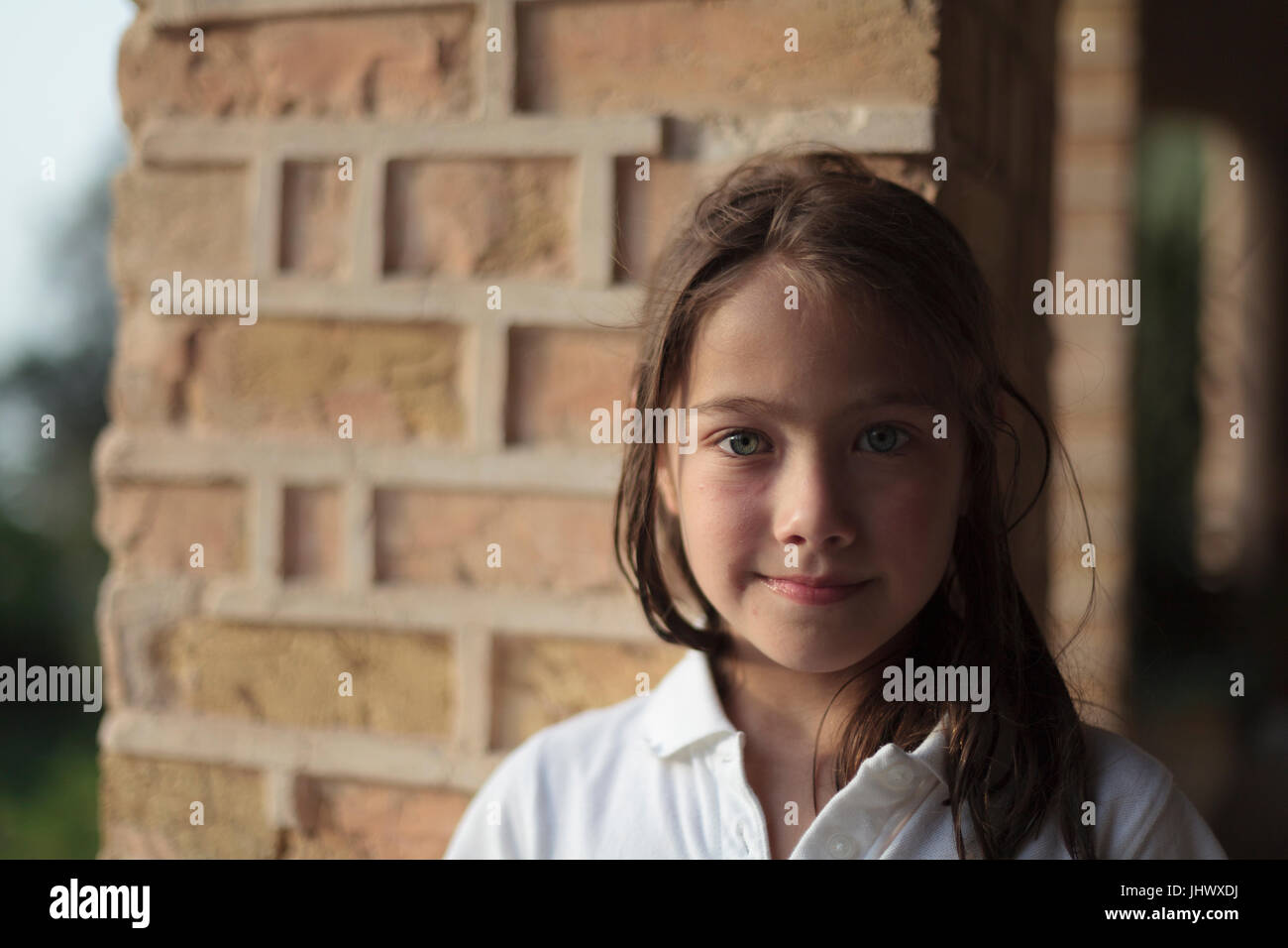 Young girls smiling with brick pillar behind her and half her face lit by sun Stock Photo