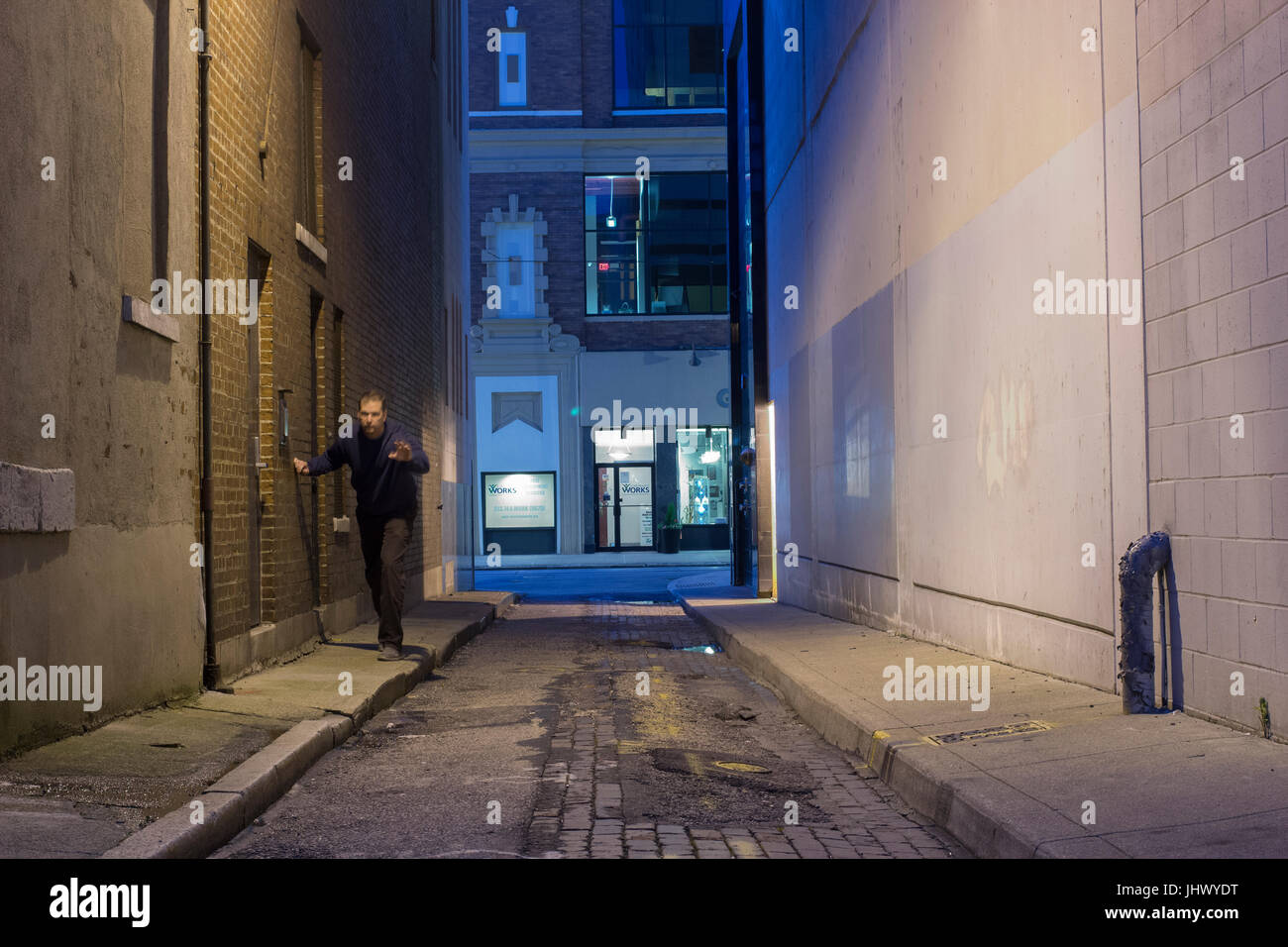 Man in a dark alley appears to be drunk, lost or needs help. Stock Photo