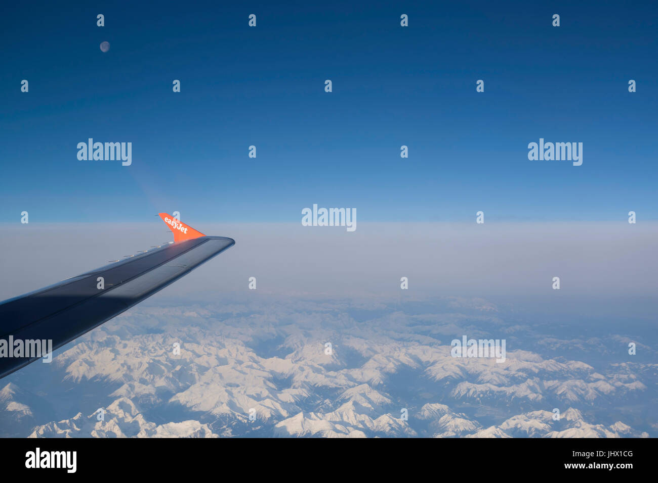 View of Easy Jet airplane wing from the window flying over the Alps, blue sky and moon Stock Photo