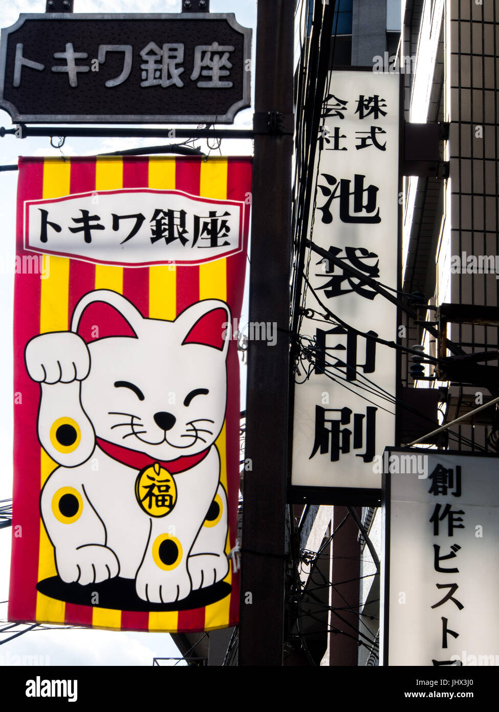 Maneki-neko on advertising banner, with kanji signs and street poles, Ikebukuro, Toko, Japan Stock Photo