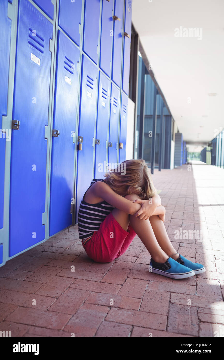 Full length of girl sitting on pavement by lockers in corridor at ...