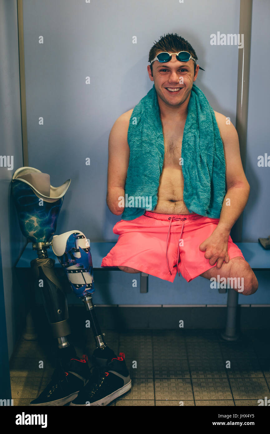 Quadriplegic swimmer in the changing cubicle. He is smiling for the camera with his prosthetic legs next to him. Stock Photo