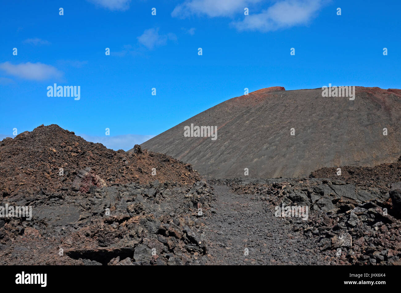 A red volcanic cone with a trekking route through a moonscape of Timanfaya National Park on Lanzarote Stock Photo