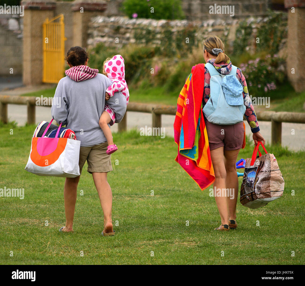 On their way to a picnic at the seaside, two grown-ups and young kiddie, with picnic bags Stock Photo