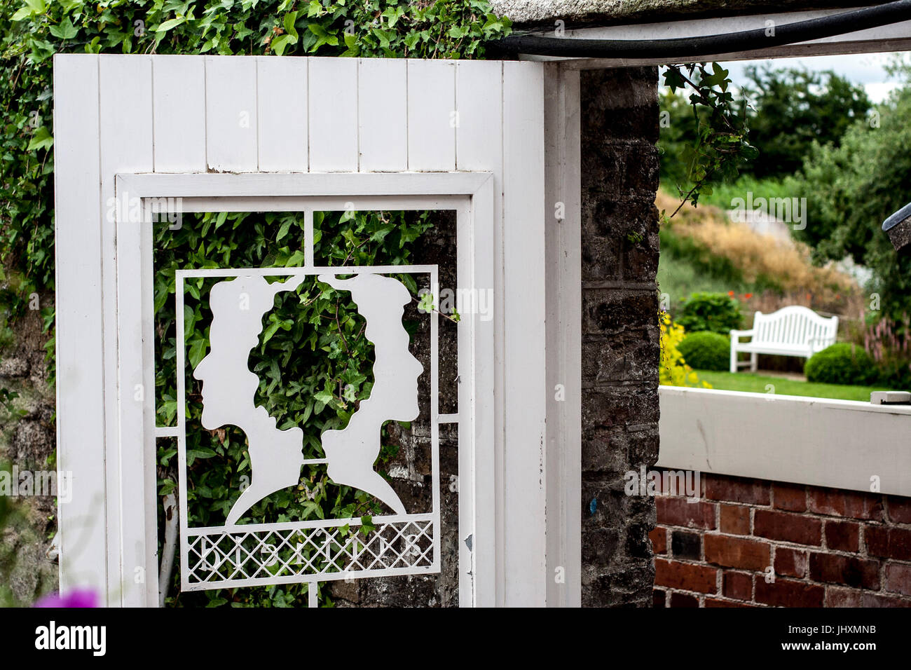 White wooden panelled garden gate with a stunning commissioned design of two female heads back to back Stock Photo