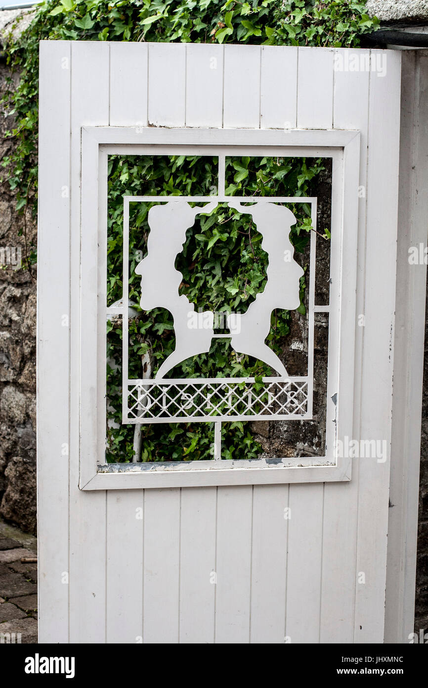 White wooden panelled garden gate with a stunning commissioned design of two female heads back to back Stock Photo