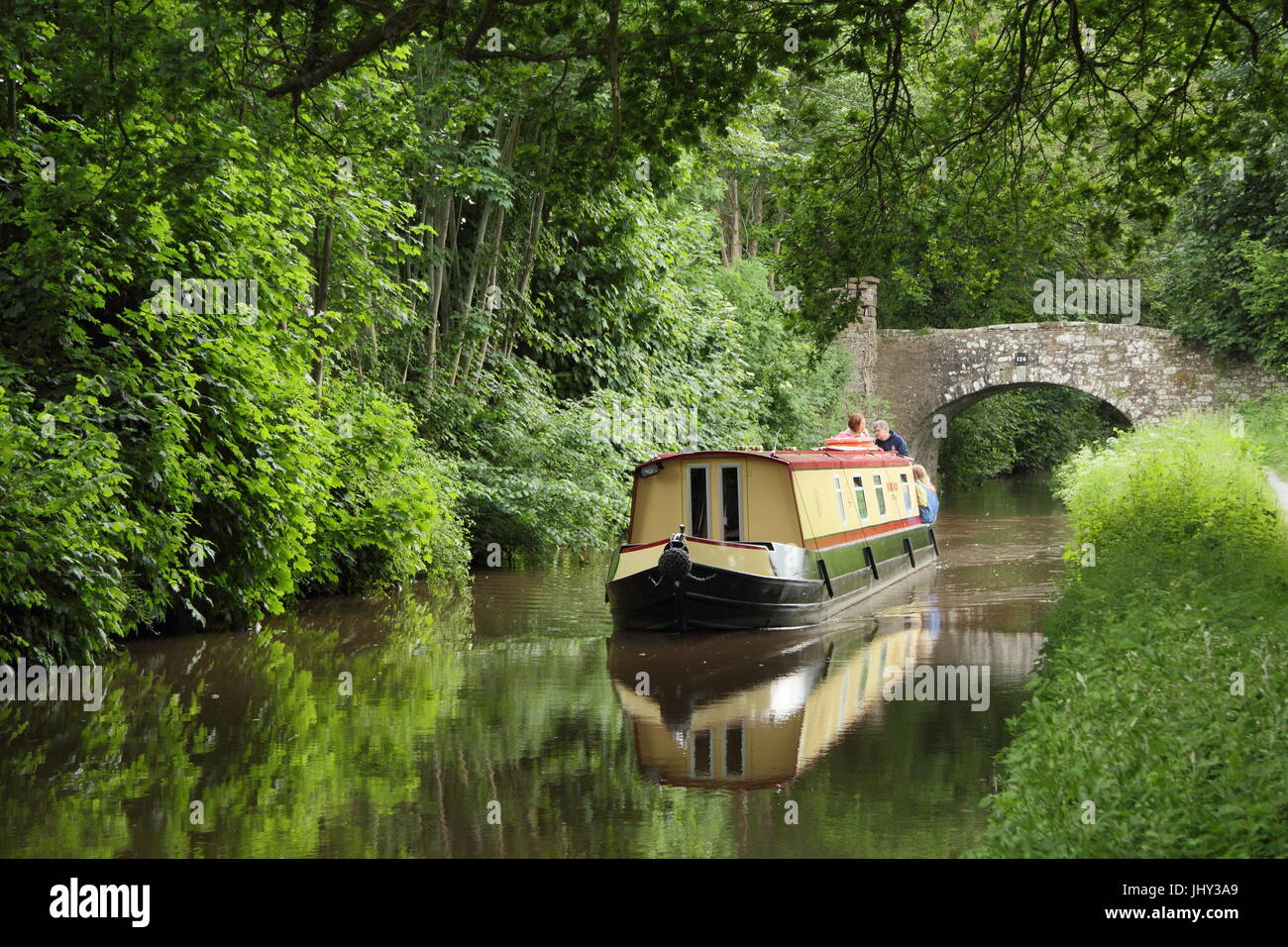 Narrowboat holiday makers navigate the Monmounthshire and Brecon Canal near Llangynidr in the Brecon Beacons, Powys, South Wales, UK - summer Stock Photo