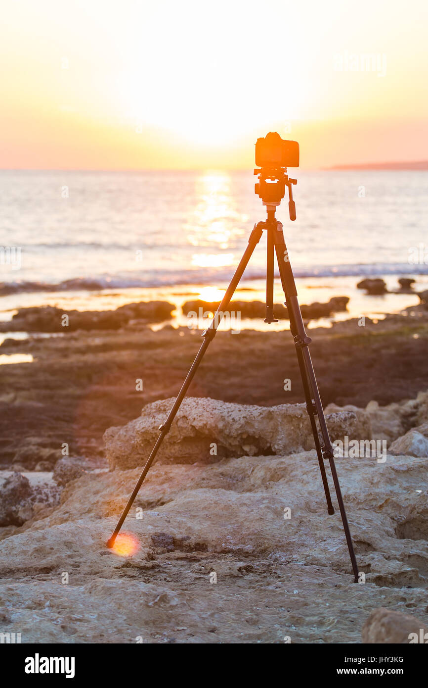 Camera with tripod over sun rising near the beach Stock Photo - Alamy