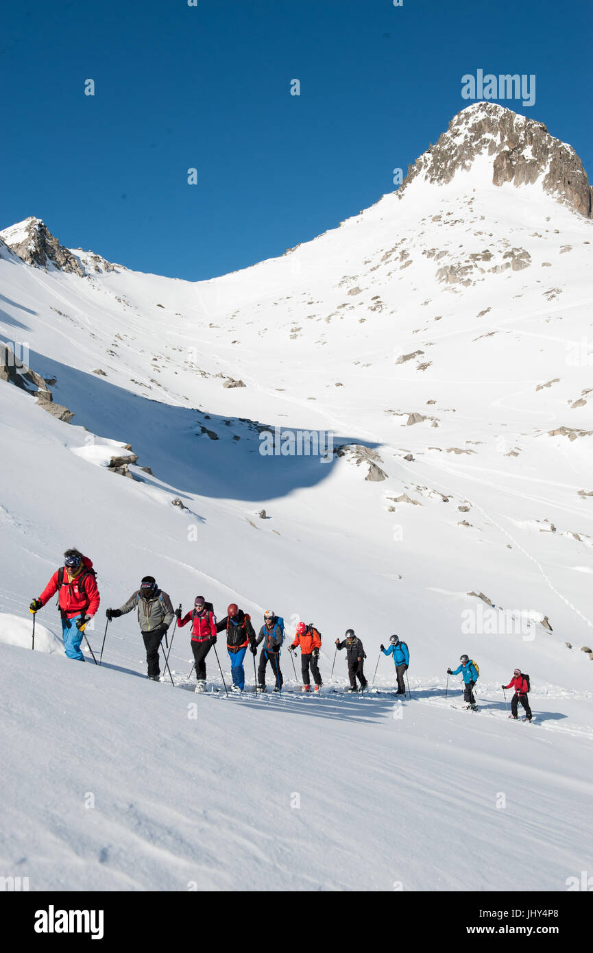 Ski tour in the mountains of the Disentis region in Switzerland. The skis are mounted on the backpacks for the climb over a steep rock face Stock Photo