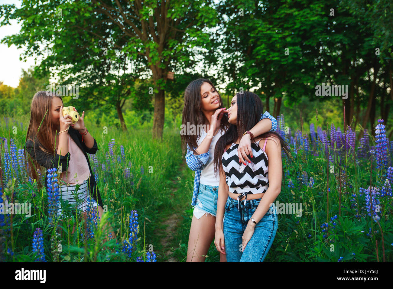 Three hipsters girls blonde and brunette taking self portrait on polaroid camera and smiling outdoor. Girls having fun together in park. Stock Photo