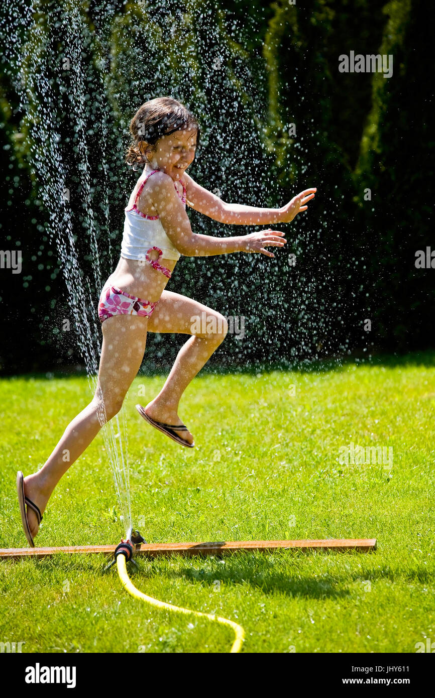 Young girl refreshes herself under the lawn sprinkler, Junges Maedchen erfrischt sich unterm Rasensprenger Stock Photo