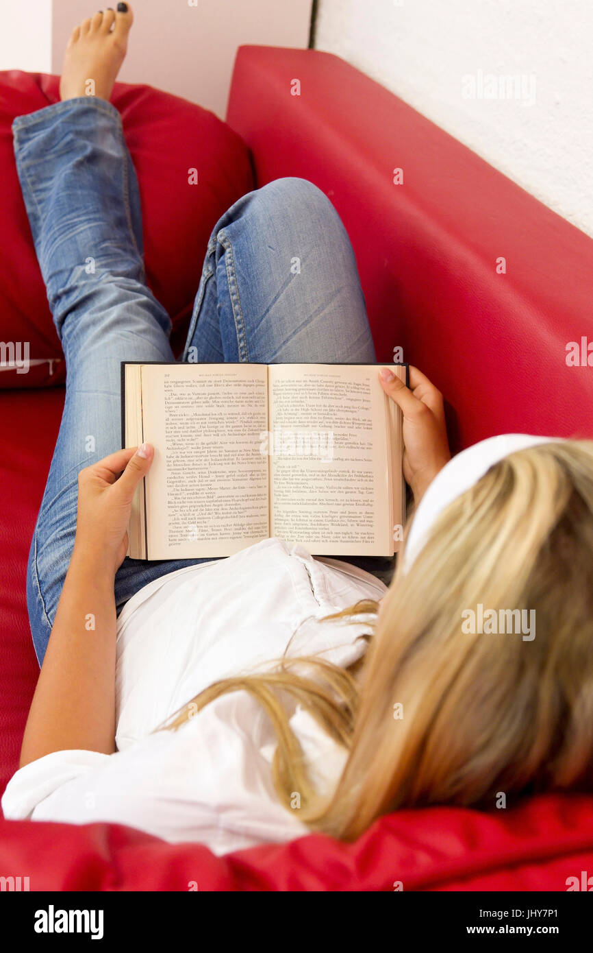 Young woman lies on sofa and reads a book - Young woman is reading a book, Junge Frau liegt auf Sofa und liest ein Buch - Young woman is reading a boo Stock Photo