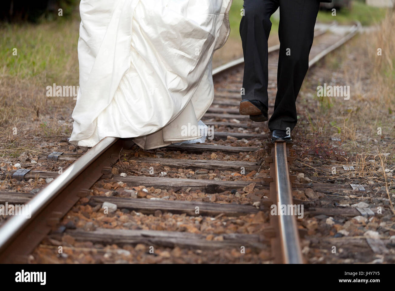Bride and groom run on rail in the railway station - bridal couple At a railway station, walking on straight, Brautpaar laufen auf Schiene am Bahnhof  Stock Photo