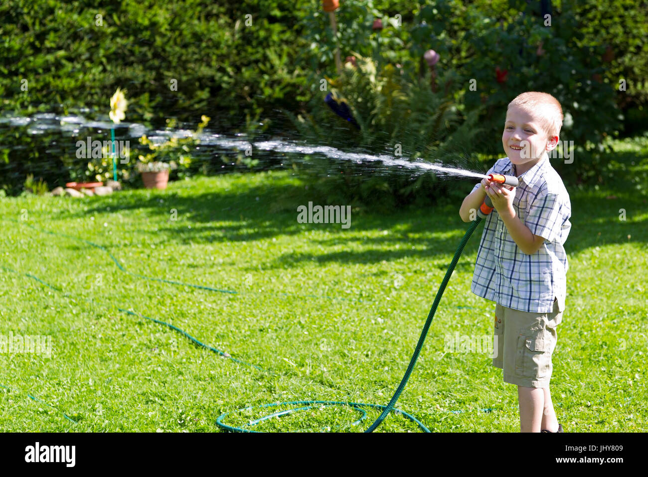 small boy plays with water hose in the garden if bellboy plays with