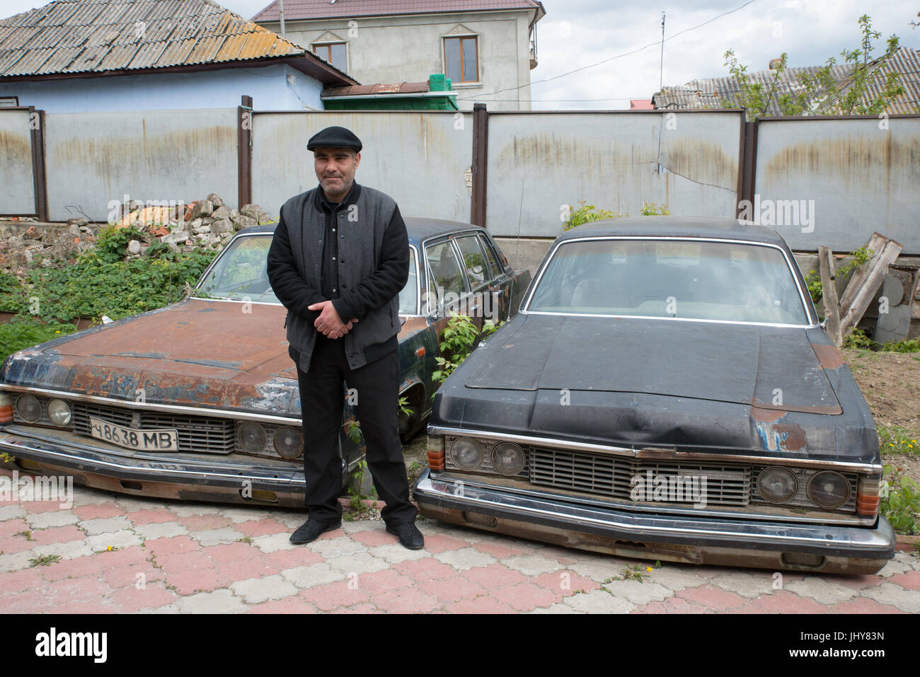 A Roma man in front of two old diplomatic cars from USSR, Soroca, Moldavia Stock Photo