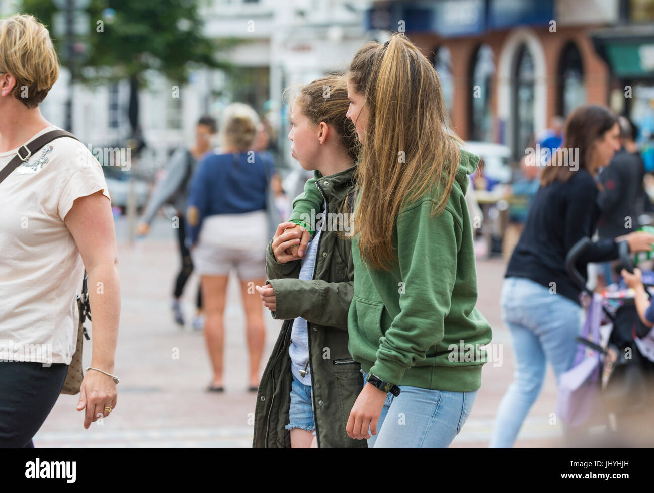 Young female friends walking along holding hands on a busy street. Stock Photo