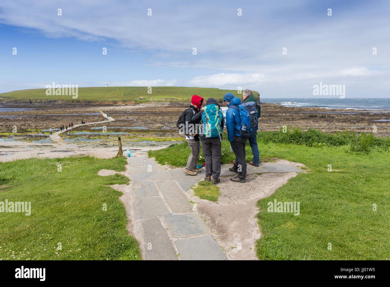 A group of tourists and walkers gather by the tidal causeway linking the Brough of Birsay with mainland Orkney, Scotland UK Stock Photo