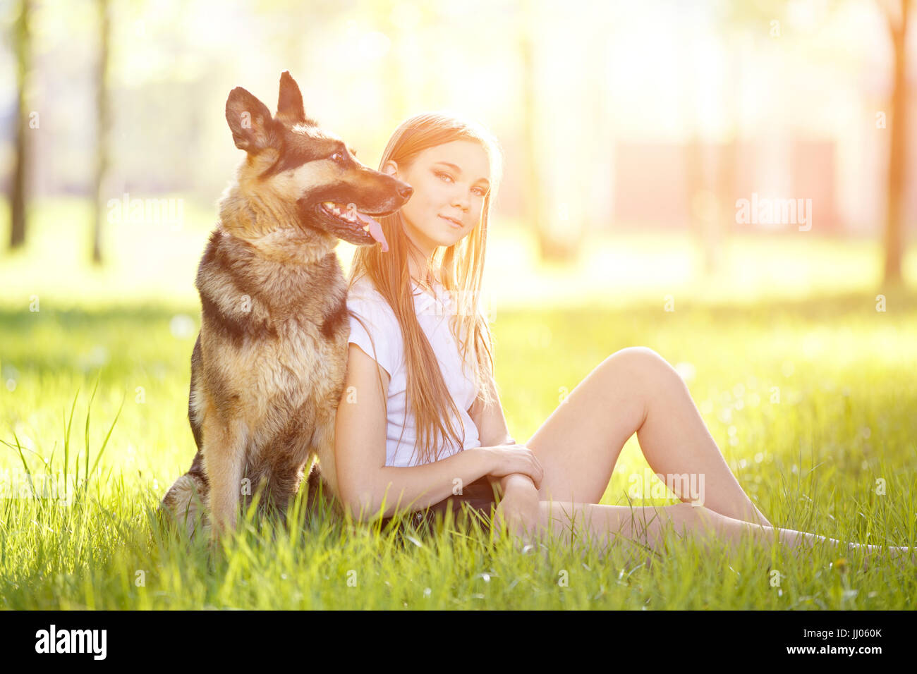 Teenage girl in white shirt with her dog sitting on grass in the park ...