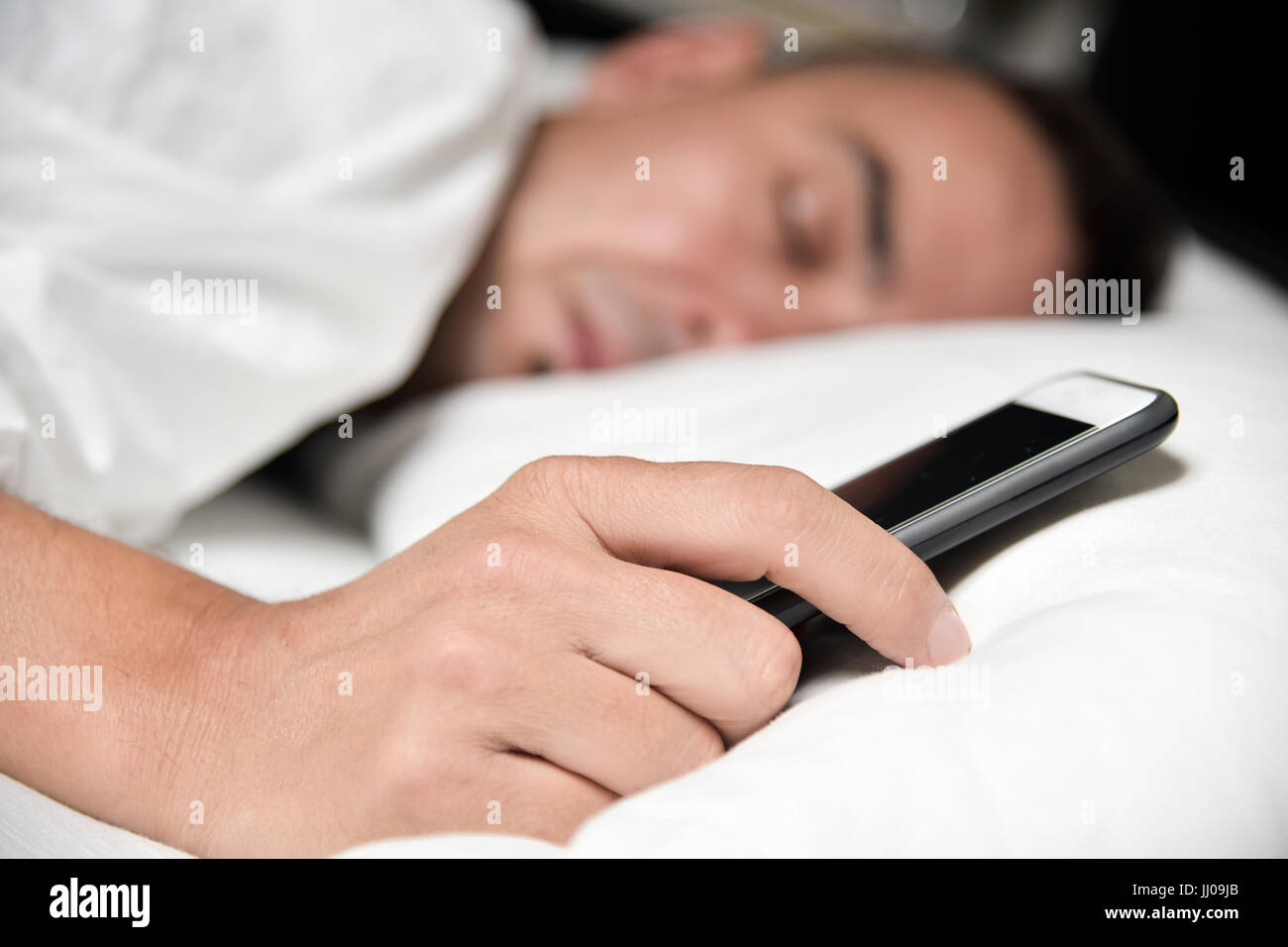closeup of a young caucasian man lying down in bed grabbing his smartphone Stock Photo