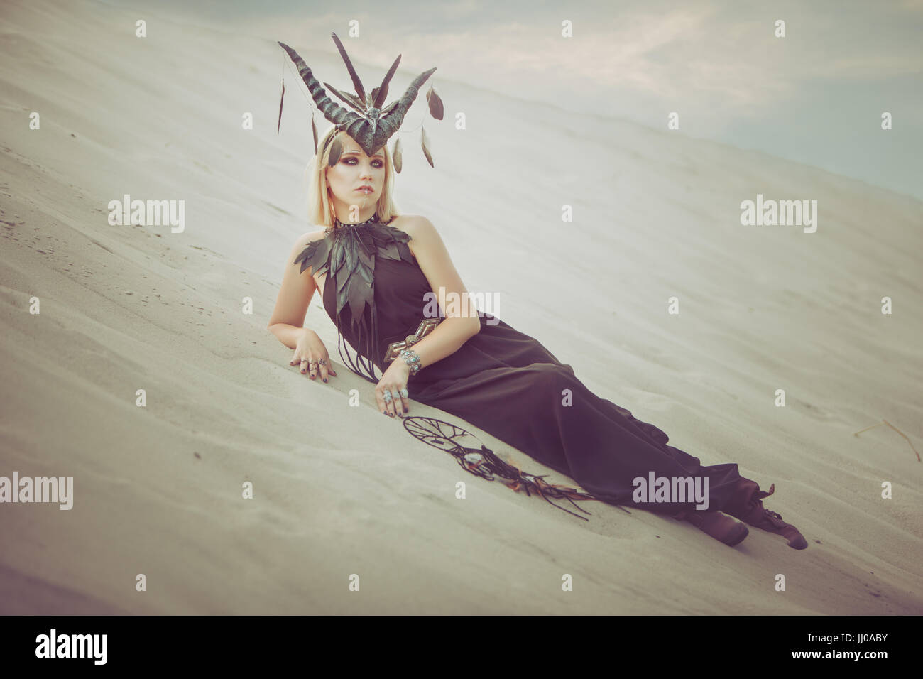 Woman with horns on her head lying on the sand in the desert. Stock Photo