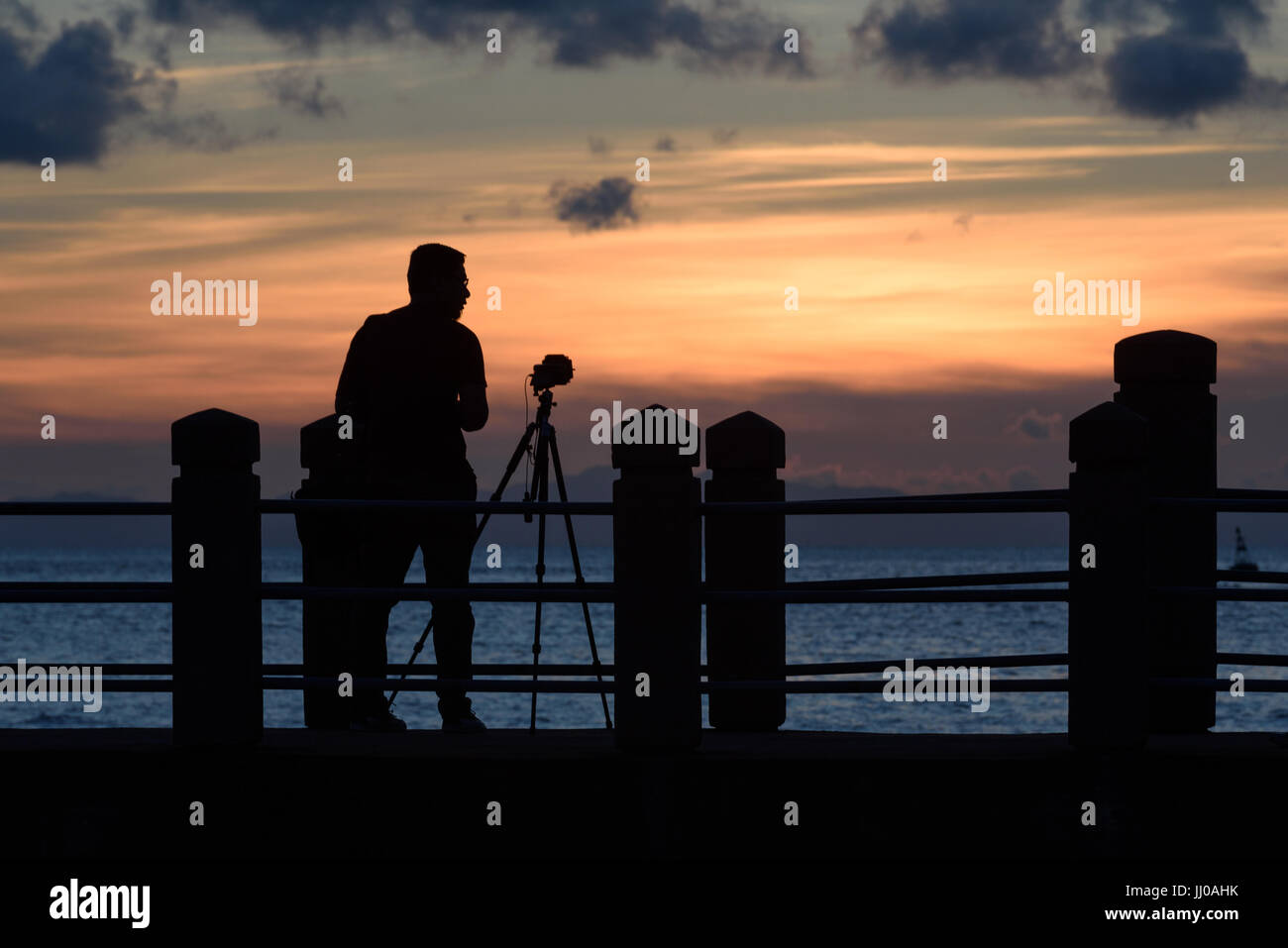A photographer with camera fixed on a tripod in silhouette during ...