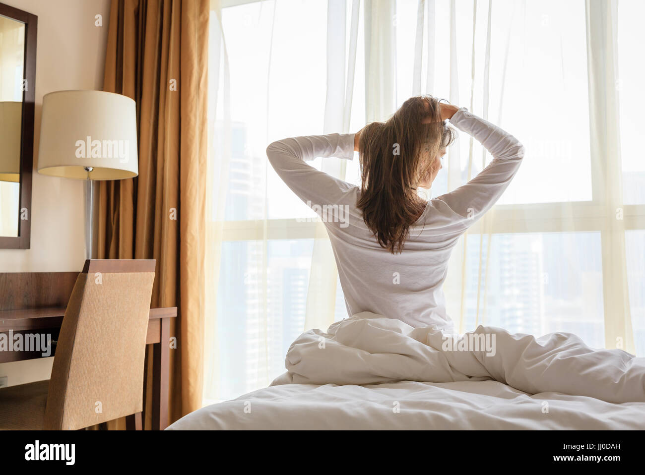 Mature woman is waking up in her bedroom in a hotel/apartment Stock Photo