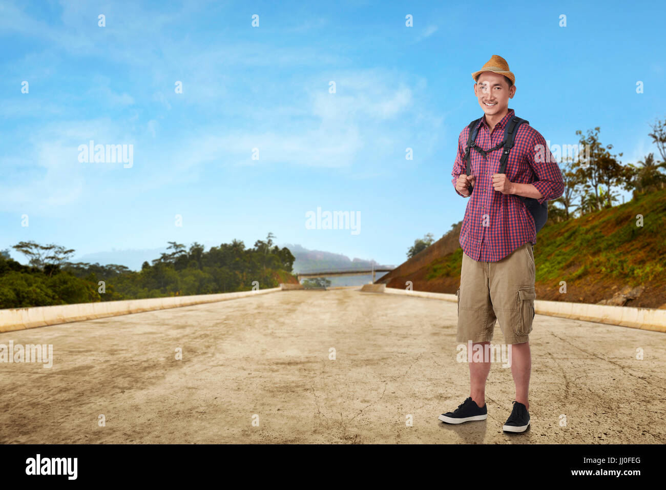 Young asian man traveling with hat and bag against landscape background Stock Photo