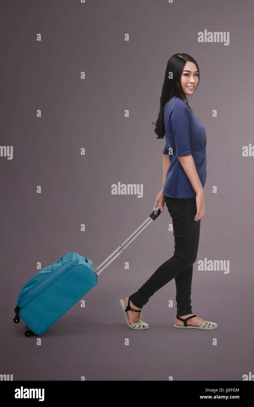Pretty asian traveler woman carrying suitcase against dark background Stock Photo