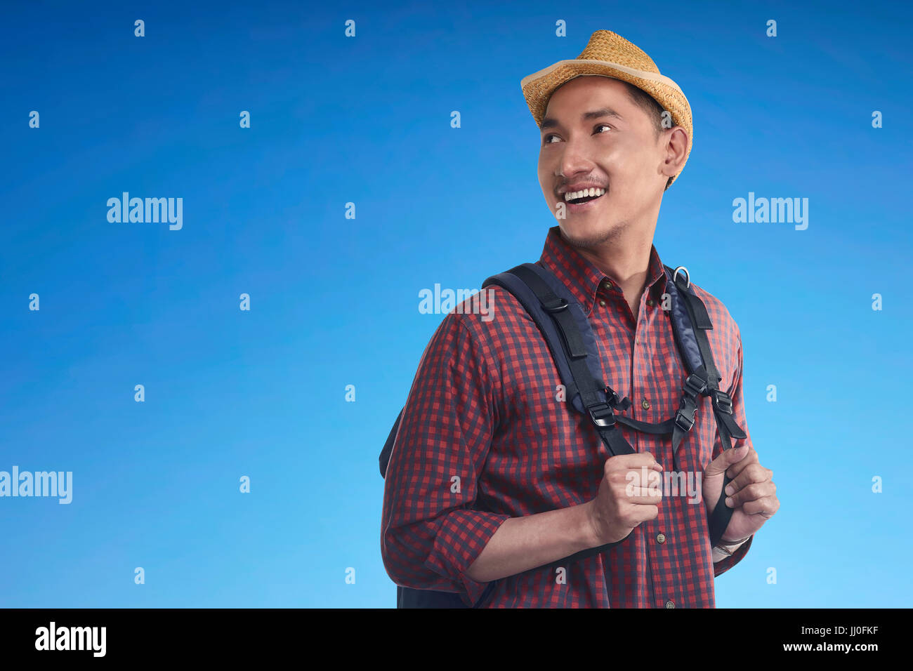 Happy asian backpacker wearing hat carrying backpack against bright ...