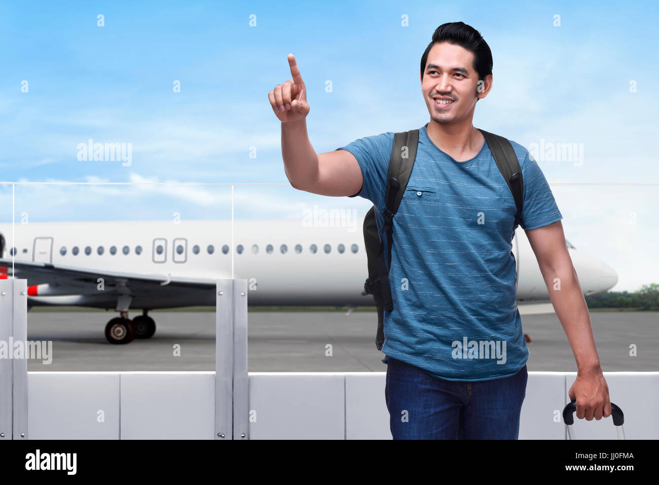 Traveler asian man with bag holding suitcase and pointing with airplane on the background Stock Photo