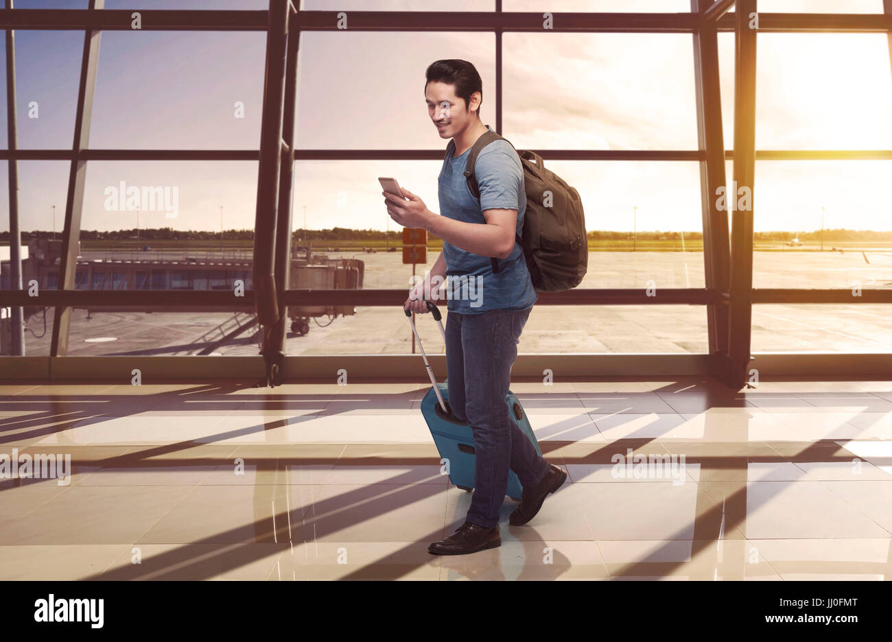 Happy asian tourist holding phone and carrying suitcase on the airport Stock Photo