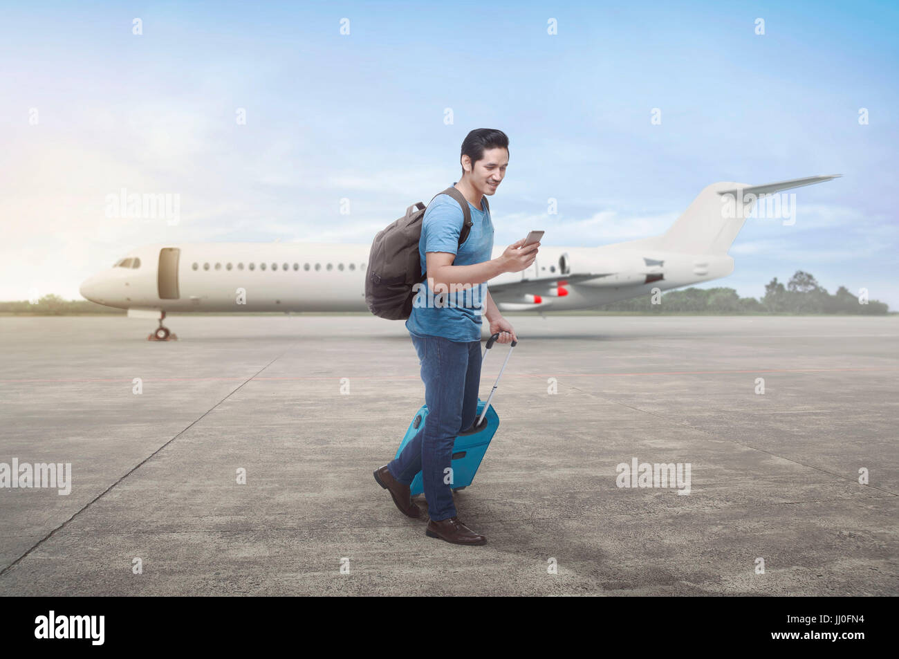 Young asian traveler walking with bags and cellphone on runway airplane Stock Photo