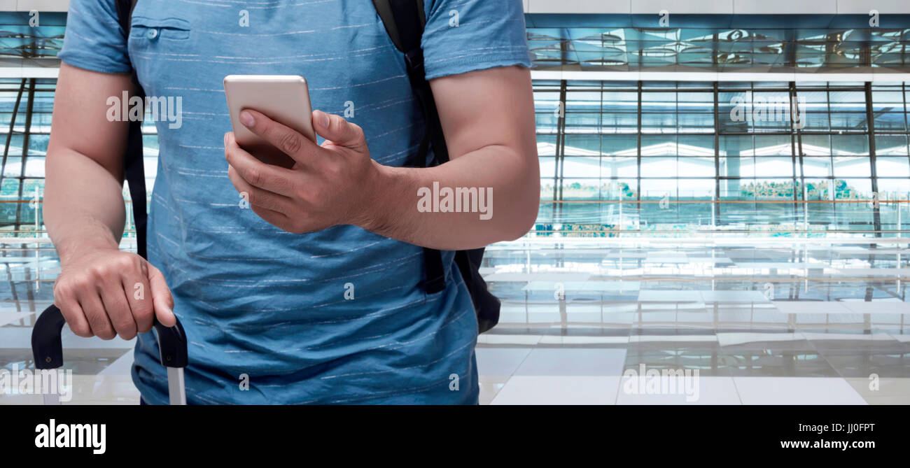 Traveler asian man with suitcase holding mobile phone in the airport terminal Stock Photo