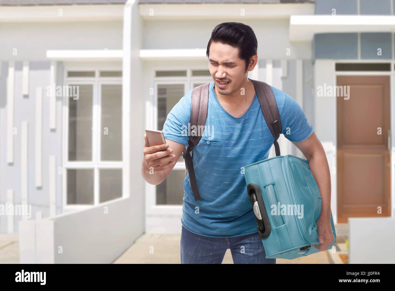 Portrait of asian traveler man running carrying suitcase with home at background Stock Photo