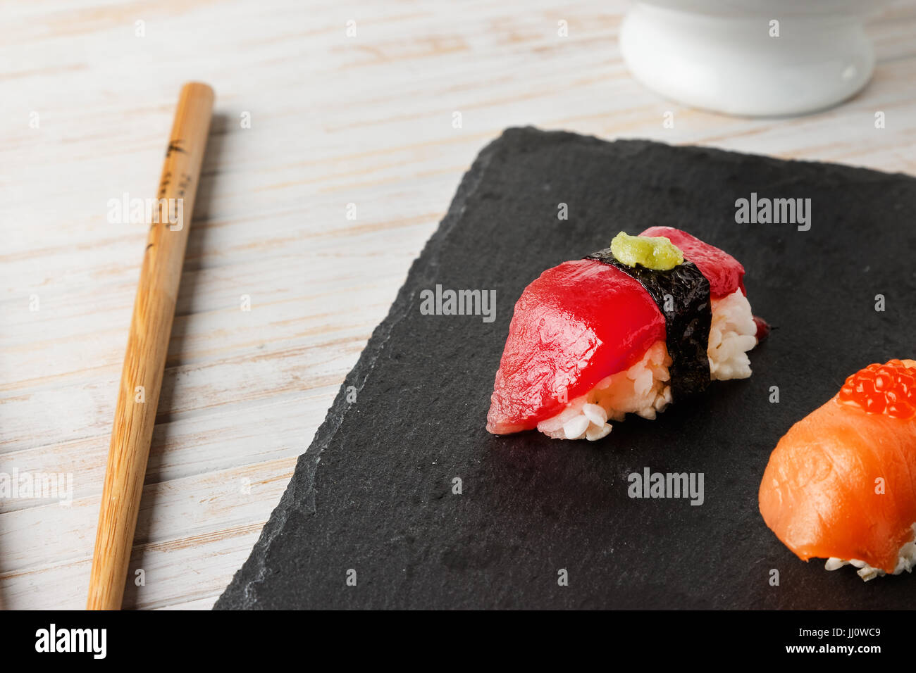 Red tuna Nigiri with Nori seaweed and wasabi paste on black slate stone with chopsticks. Raw fish in traditional Japanese sushi style. Horizontal imag Stock Photo