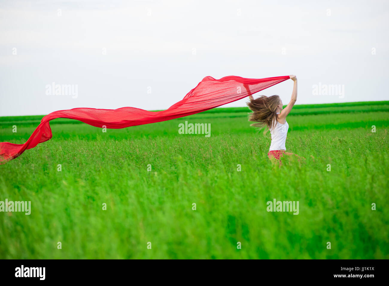 Young lady runing with tissue in green field. Woman with scarf. Stock Photo