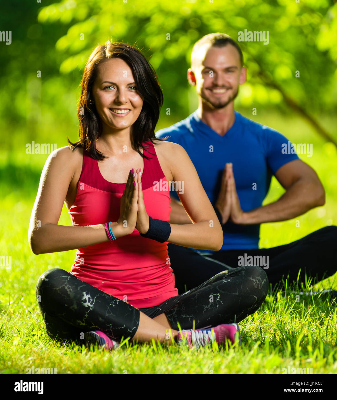 Young man and woman doing yoga in the sunny summer park Stock Photo
