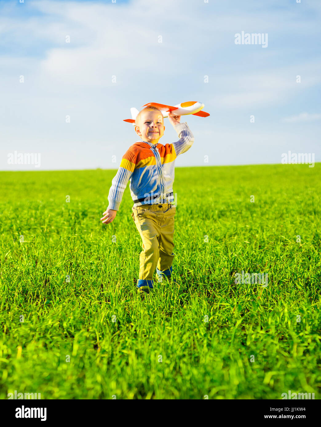 Happy boy playing with toy airplane against blue summer sky and green ...