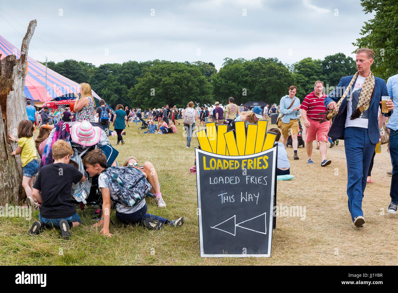 Loaded fries sign, with man in suit and scarf with beer looking suspiciously at children investigating backpack on buggy. Latitude Festival, Suffolk Stock Photo