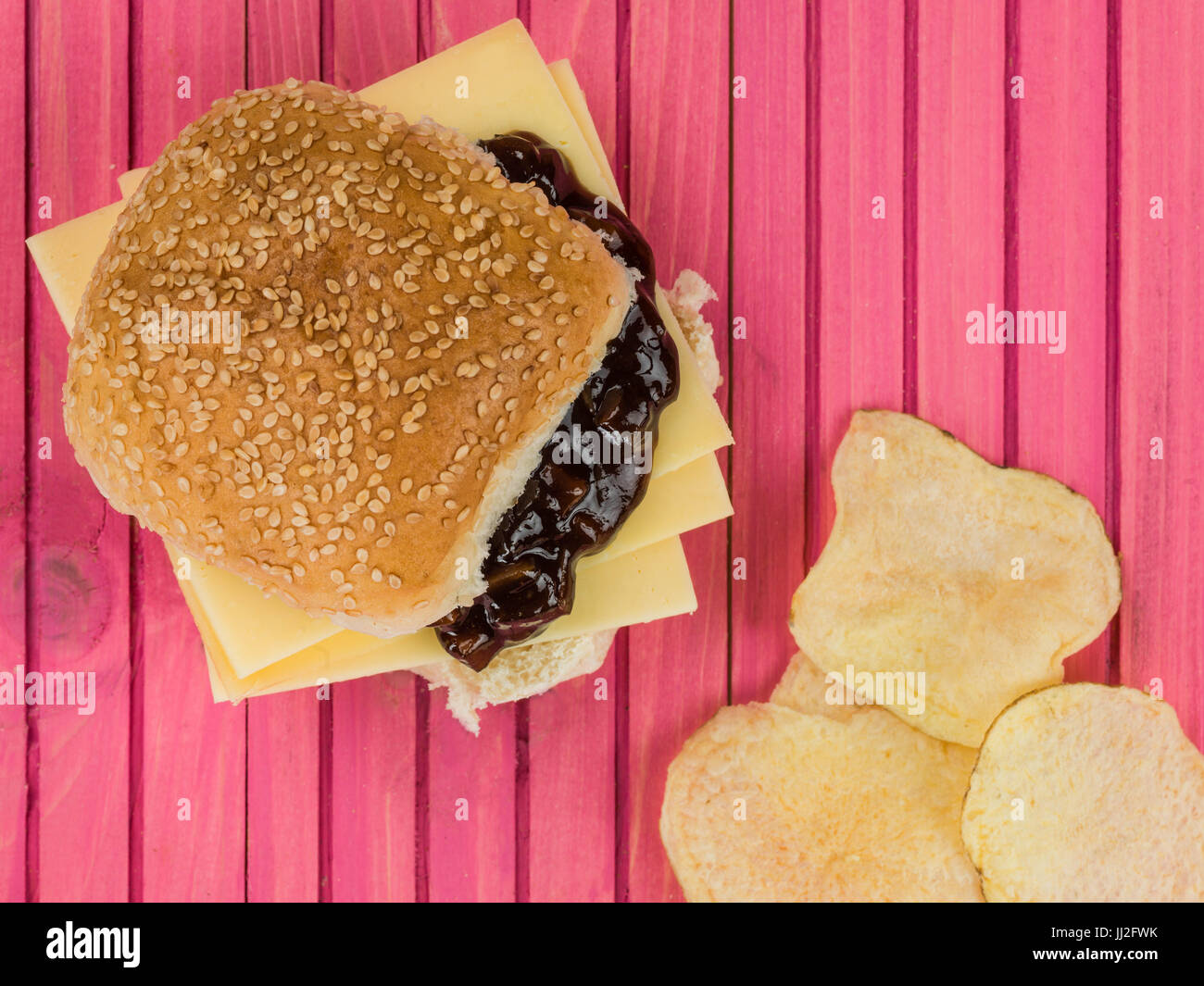 Cheese and Pickle Sesame Bread Roll With Potato Crisps Against a Pink
