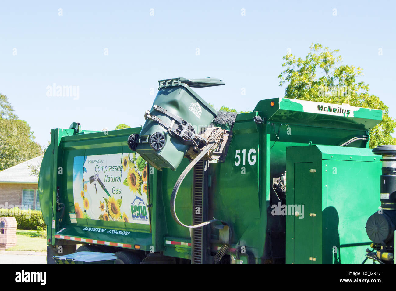 A garbage truck lifting up a green trashcan. Stock Photo