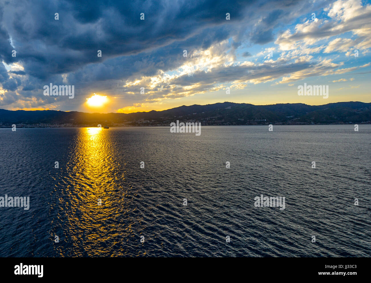 The sun's rays shine on a lone boat at sunset along the Sicilian Coast ...