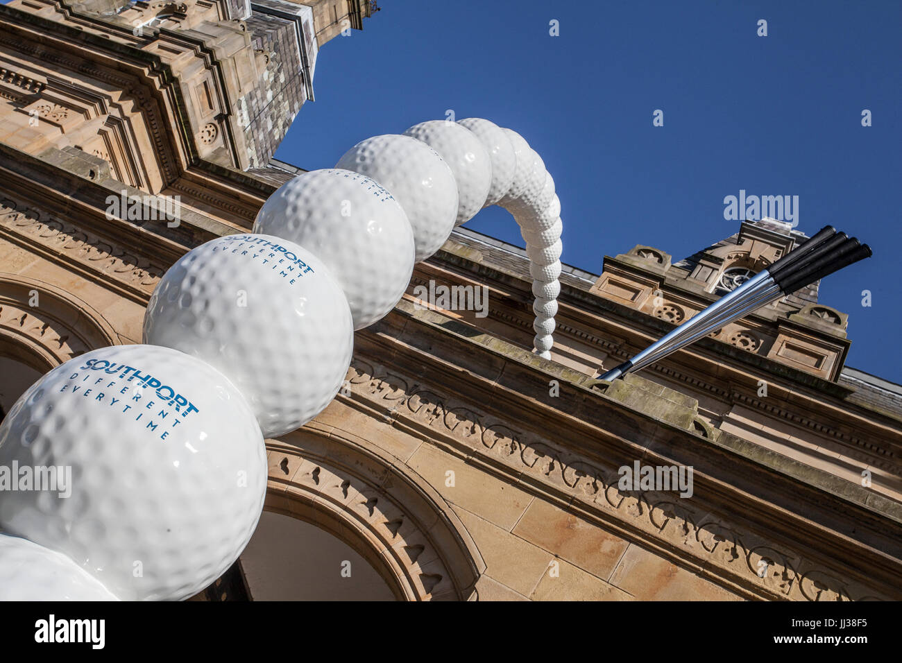 Giant statue of golf clubs, which replicate the motion of a swing,  20 golf balls placed at the top of a building on Lord Street, Southport descending down into a golf green hole. A Golf ball themed art sculpture & mini-golf, putting green, pitch & put gardens open ahead of the 146th Open Golf Championship on the 20th July. Golf clubs, replicating the motion of a swing, a masterpiece golfing artwork inspired by every golfers dream, a hole in one. Stock Photo